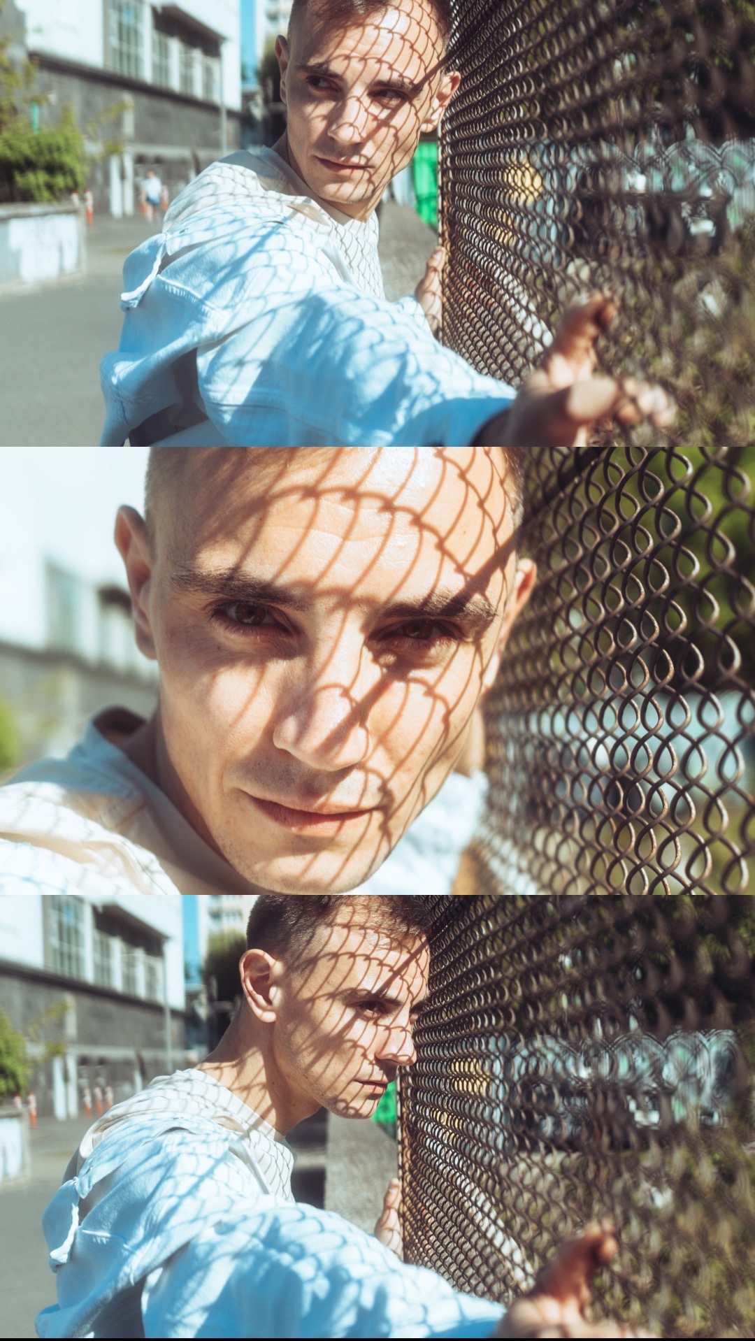 Portret młodego mężczyzny opierającego się o metalową siatkę, z cieniem siatki na twarzy, w tle budynki i ulica.
