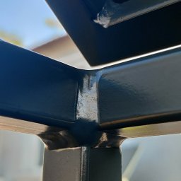 KONSTRUKCJE SZEWCZUK Vasyl Shevchuk - Szczegółowe zbliżenie na spawany narożnik metalowej konstrukcji, prawdopodobnie pergoli, ukazujący precyzyjne połączenie elementów, z widocznymi śladami spawania i świeżym lakierem w kolorze...