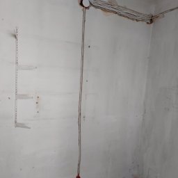 Kamiński Dariusz - Ściana w trakcie remontu z widocznymi przewodami elektrycznymi, puszką instalacyjną, listwą do półek i śladami po szpachlowaniu.