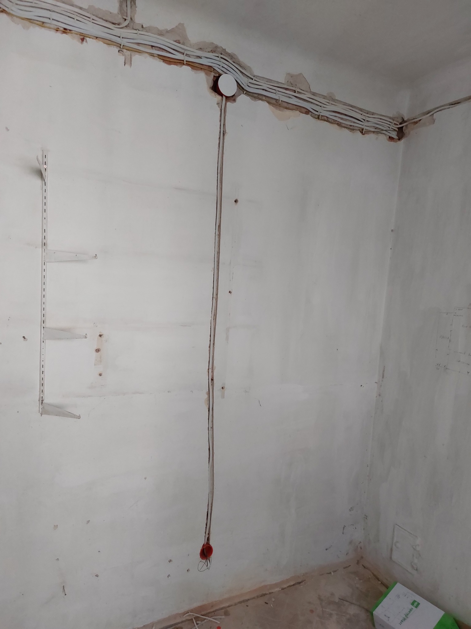 Ściana w trakcie remontu z widocznymi przewodami elektrycznymi, puszką instalacyjną, listwą do półek i śladami po szpachlowaniu.