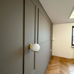 Marciniak Remonty Damian Marciniak - Panelowana ściana w odcieniach szarości z oświetleniem punktowym i parkietem ułożonym w jodełkę. Nowoczesny design wnętrza z dbałością o detale.