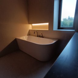 Marciniak Remonty Damian Marciniak - Minimalistyczna łazienka z wolnostojącą wanną podświetloną od góry, okno z widokiem na zieleń. Stonowana kolorystyka, nowoczesny design.