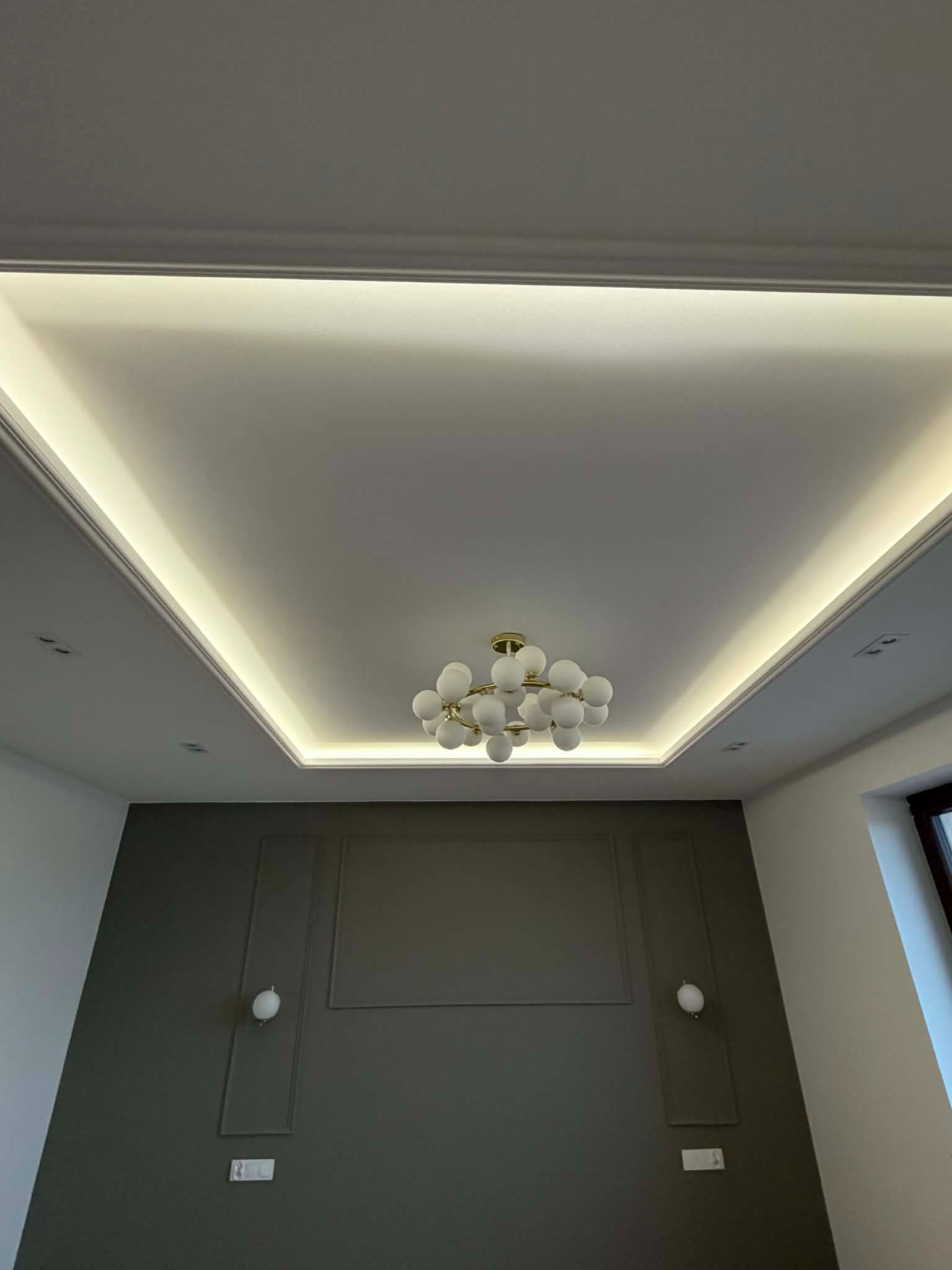 Nowoczesny sufit podwieszany z oświetleniem LED i dekoracyjną lampą w kształcie kuli, szara ściana z ozdobnymi panelami i kinkietami. Wykończenie wnętrza.