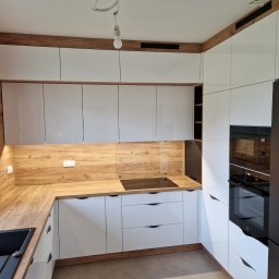 FHUP MARLON-MEBLE - Nowoczesna kuchnia w Tarnowie z białymi, lakierowanymi frontami i drewnianymi akcentami, widoczna czarna, minimalistyczna armatura zlewozmywakowa i płyta indukcyjna.