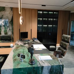 FHUP MARLON-MEBLE - Biuro z blatem biurka z zielonego marmuru, drewnianymi szafami w tle i designerskim oświetleniem.