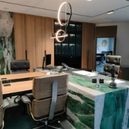 Nowoczesne biuro z dużym biurkiem z zielonego marmuru, drewnianymi szafami w tle i designerskim oświetleniem sufitowym.