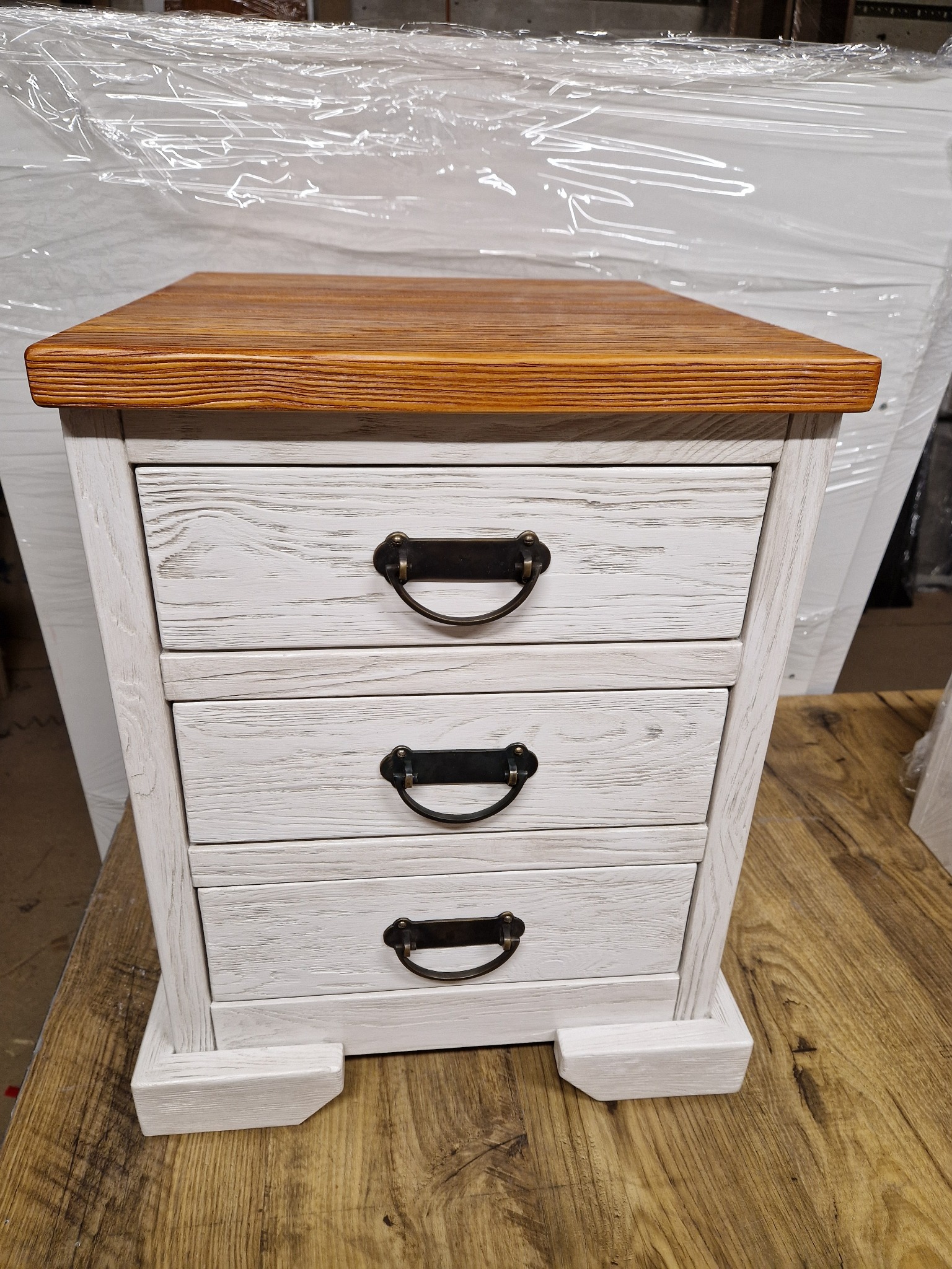 Drewniana szafka nocna z trzema szufladami, bielona z brązowym blatem, uchwyty w stylu retro.