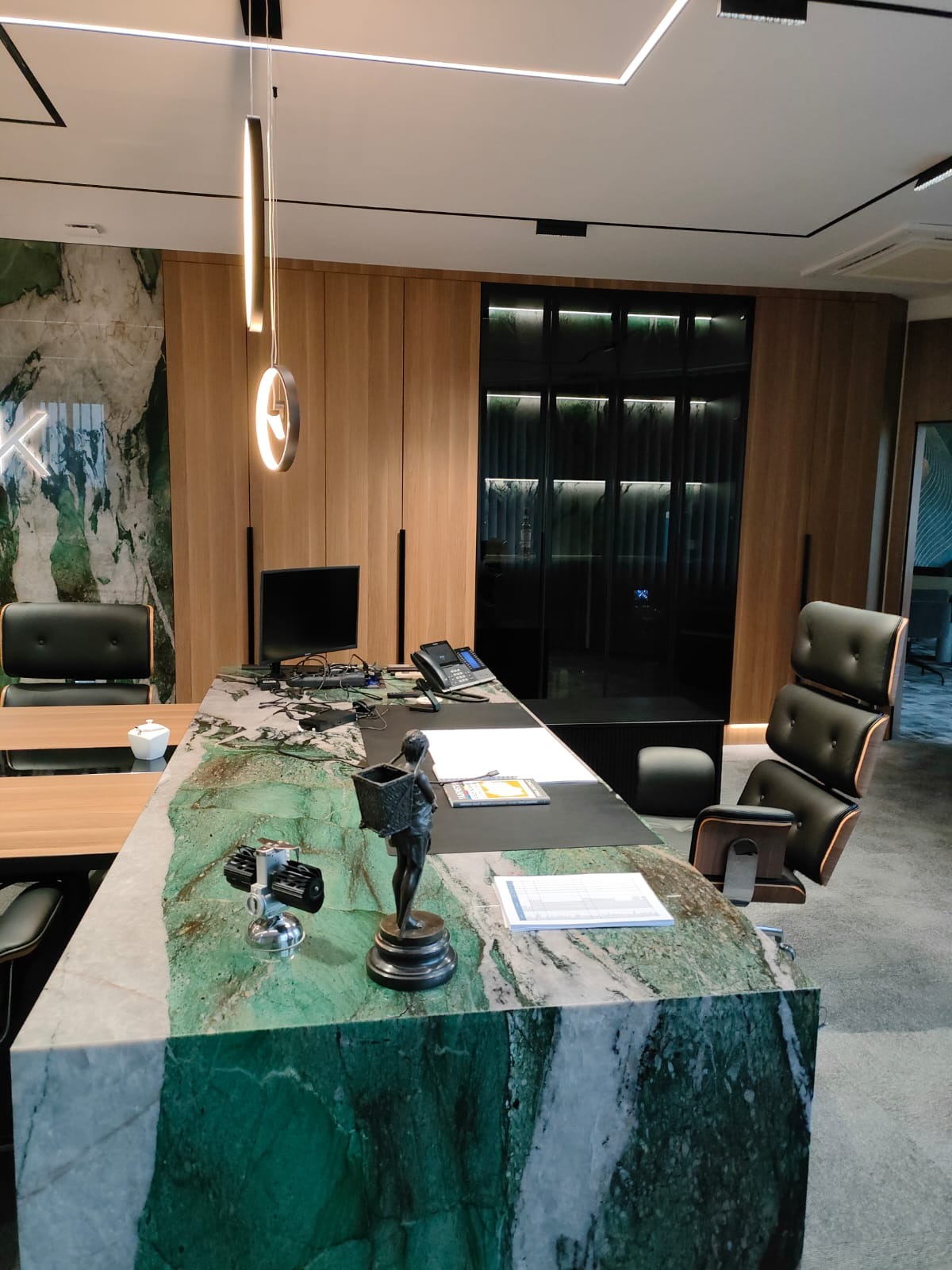 Biuro z blatem biurka z zielonego marmuru, drewnianymi szafami w tle i designerskim oświetleniem.