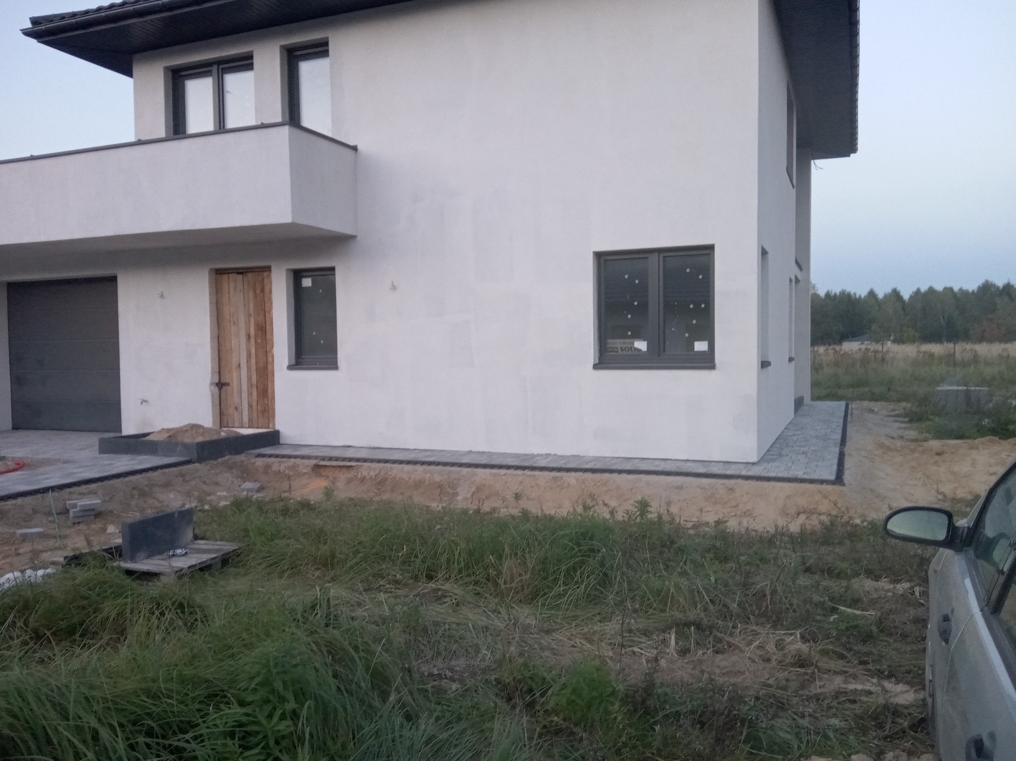 Nowoczesny dom z szarą kostką brukową wokół, widoczne przygotowania do dalszych prac ziemnych.