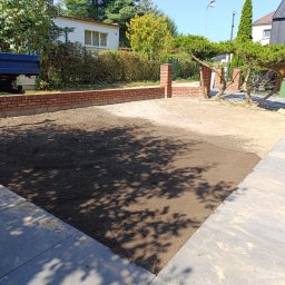 Ogrody Perfecto - Przygotowany teren pod trawnik z widoczną świeżo ułożoną ziemią, obrzeżami z kostki i fragmentem murku z cegły. W tle budynki i zieleń.