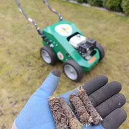 Ogrody Perfecto - Aerator do trawy w tle, w dłoni rdzenie glebowe. Napowietrzanie trawnika, poprawa drenażu i wzrostu trawy. Wertykulacja trawnika.