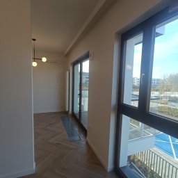 Roman Plikhivskyi - Wnętrze mieszkania po remoncie: parkiet ułożony w jodełkę, duże okna balkonowe z widokiem na zewnątrz, nowoczesna lampa sufitowa.