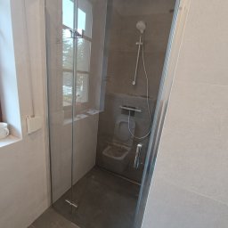 Roman Plikhivskyi - Kabina prysznicowa ze szklanymi drzwiami w nowoczesnej łazience w Warszawie, widoczny sedes podtynkowy i szara glazura.