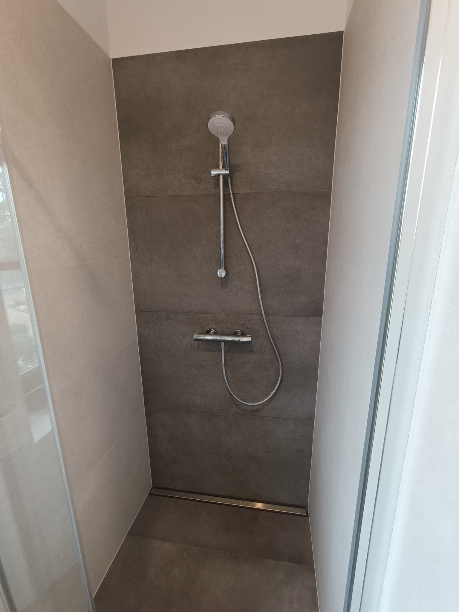 Nowoczesny prysznic typu walk-in z szarą, poziomą glazurą, chromowaną armaturą i odpływem liniowym w podłodze.