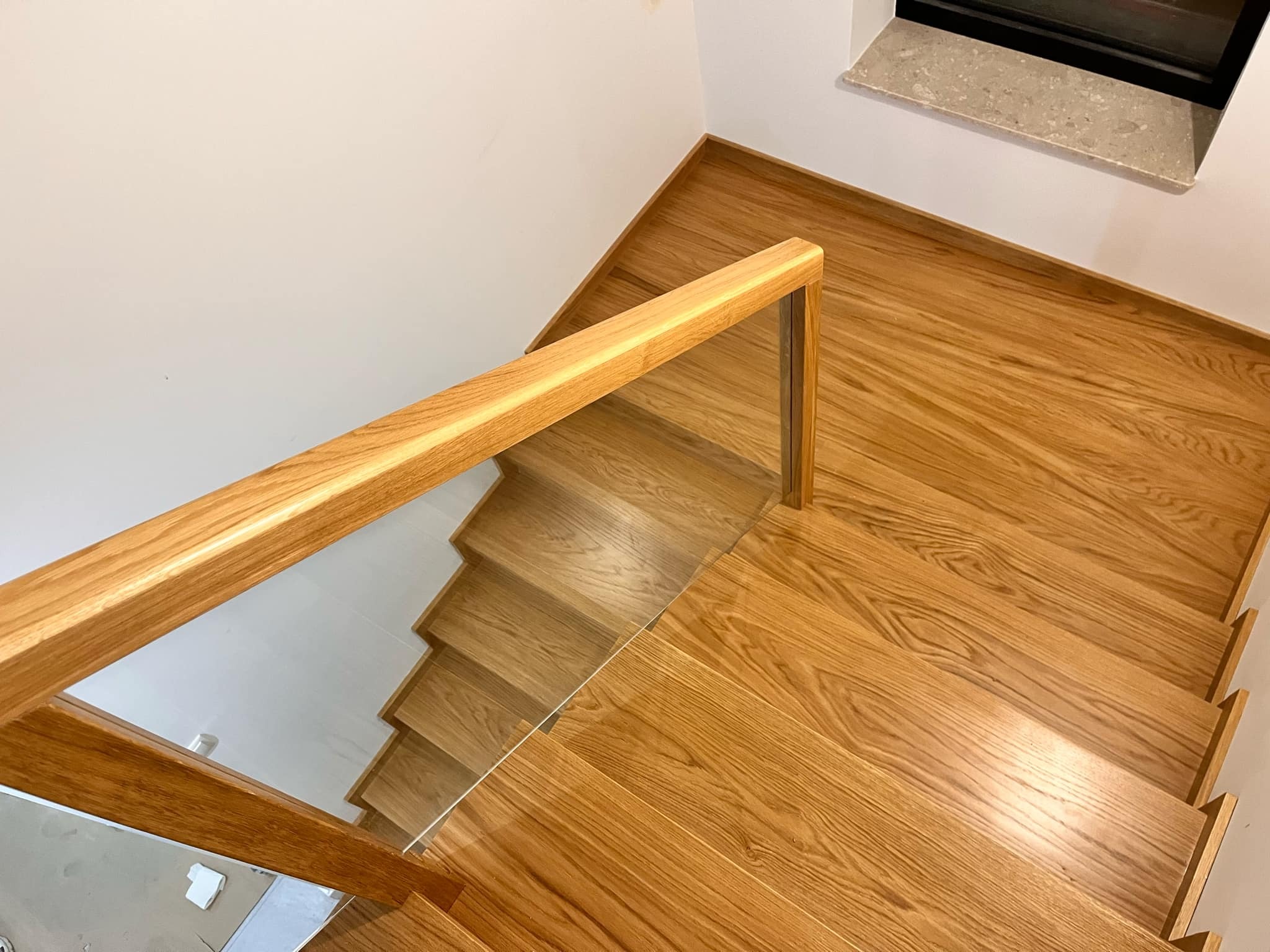 Nowoczesne schody z jasnego drewna z balustradą szklaną i drewnianym poręczą, widok z góry, podkreślający naturalne usłojenie drewna i minimalistyczny design.