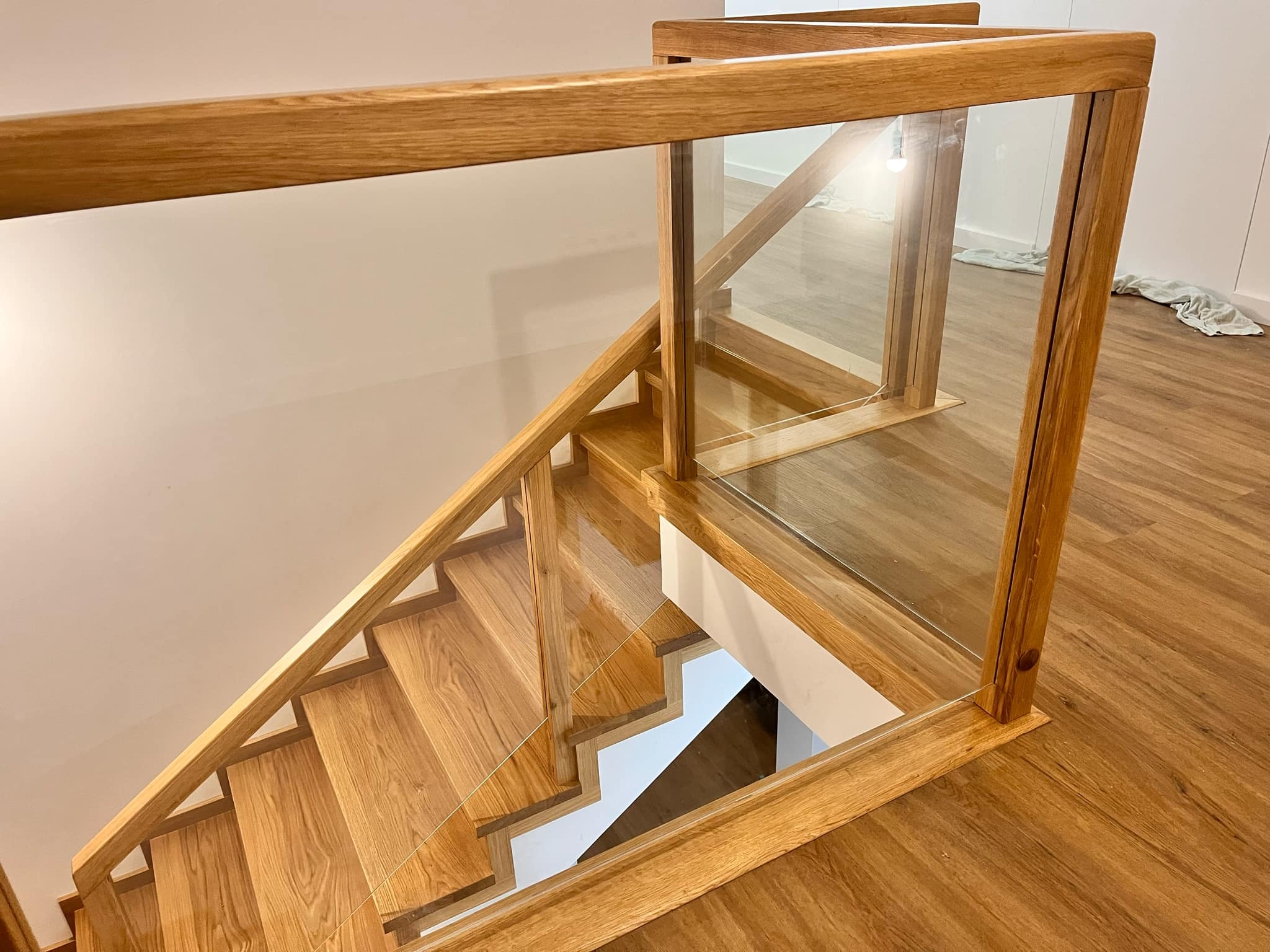 Jasne, drewniane schody z balustradą ze szkła i drewna, widziane z góry. Naturalne światło podkreśla strukturę drewna i minimalistyczny design.