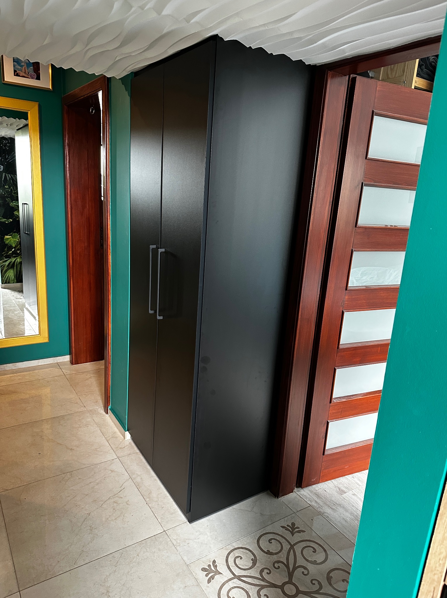 Nowoczesna aranżacja wnętrza z czarną szafą wnękową, drewnianymi drzwiami z szybami i marmurową podłogą, uzupełniona dekoracyjnym sufitem i zielonymi ścianami.