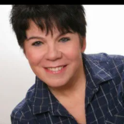 Portret uśmiechniętej kobiety w niebieskiej koszuli w kratę z krótkimi ciemnymi włosami, zrzut ekranu z Facebooka.