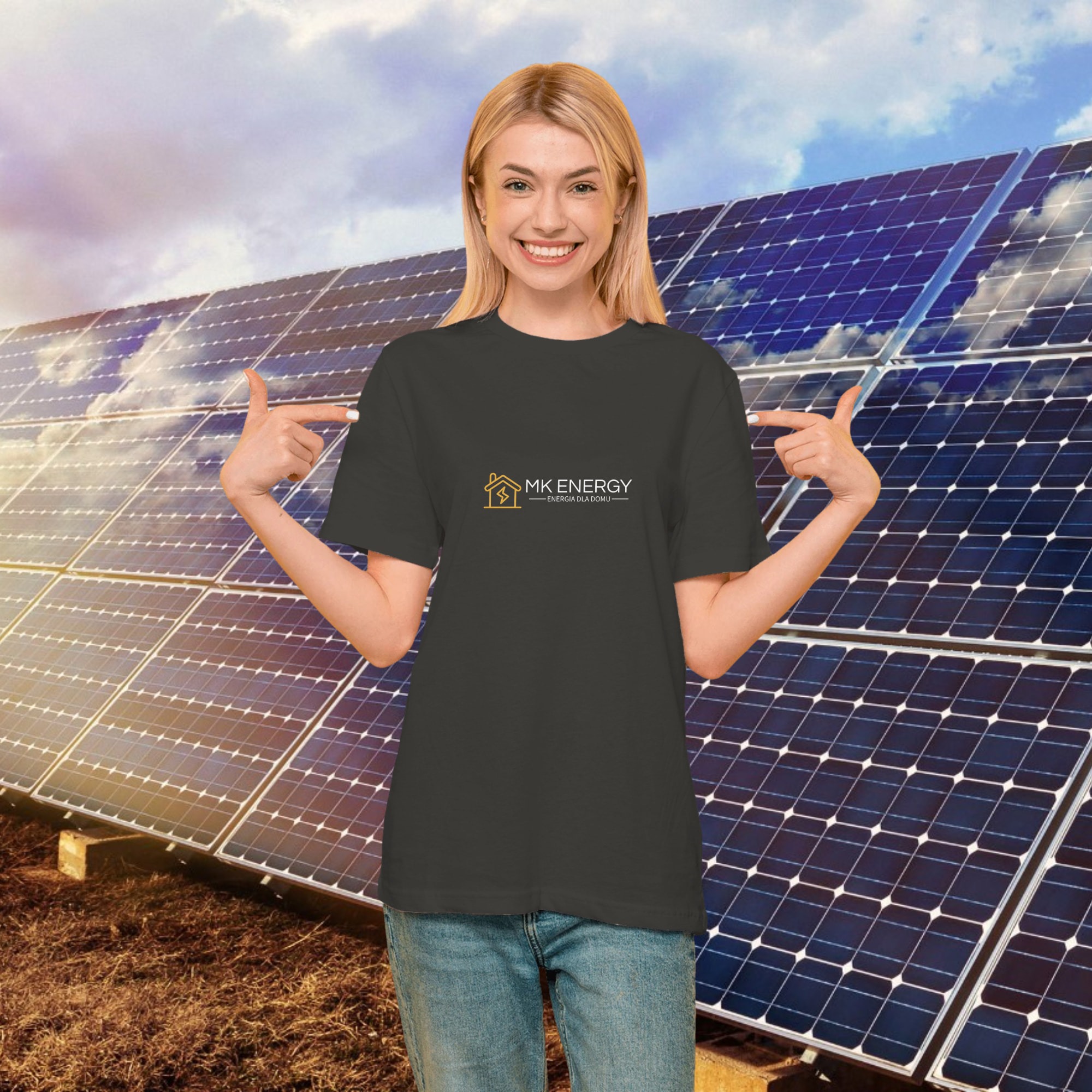 Uśmiechnięta blondynka w szarej koszulce z logo MK Energy na tle paneli fotowoltaicznych, wskazująca palcami na logo firmy.