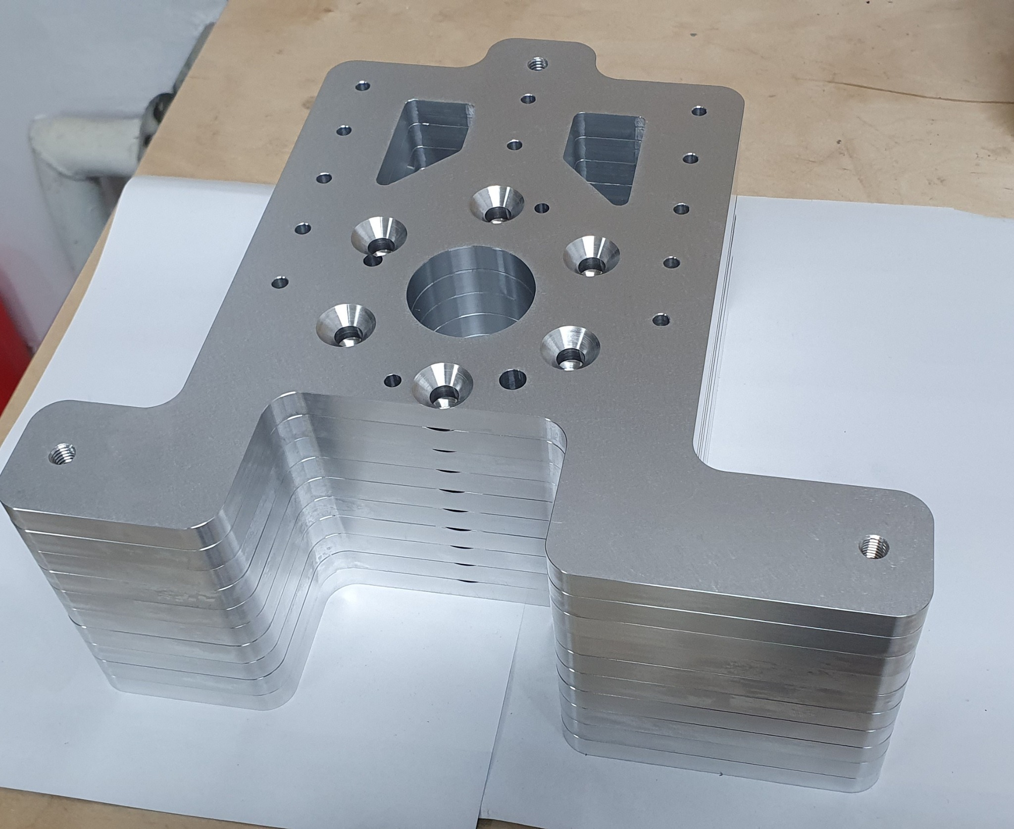 Stos srebrnych, metalowych elementów z otworami różnej wielkości, ułożonych jeden na drugim, widoczne ślady po obróbce.