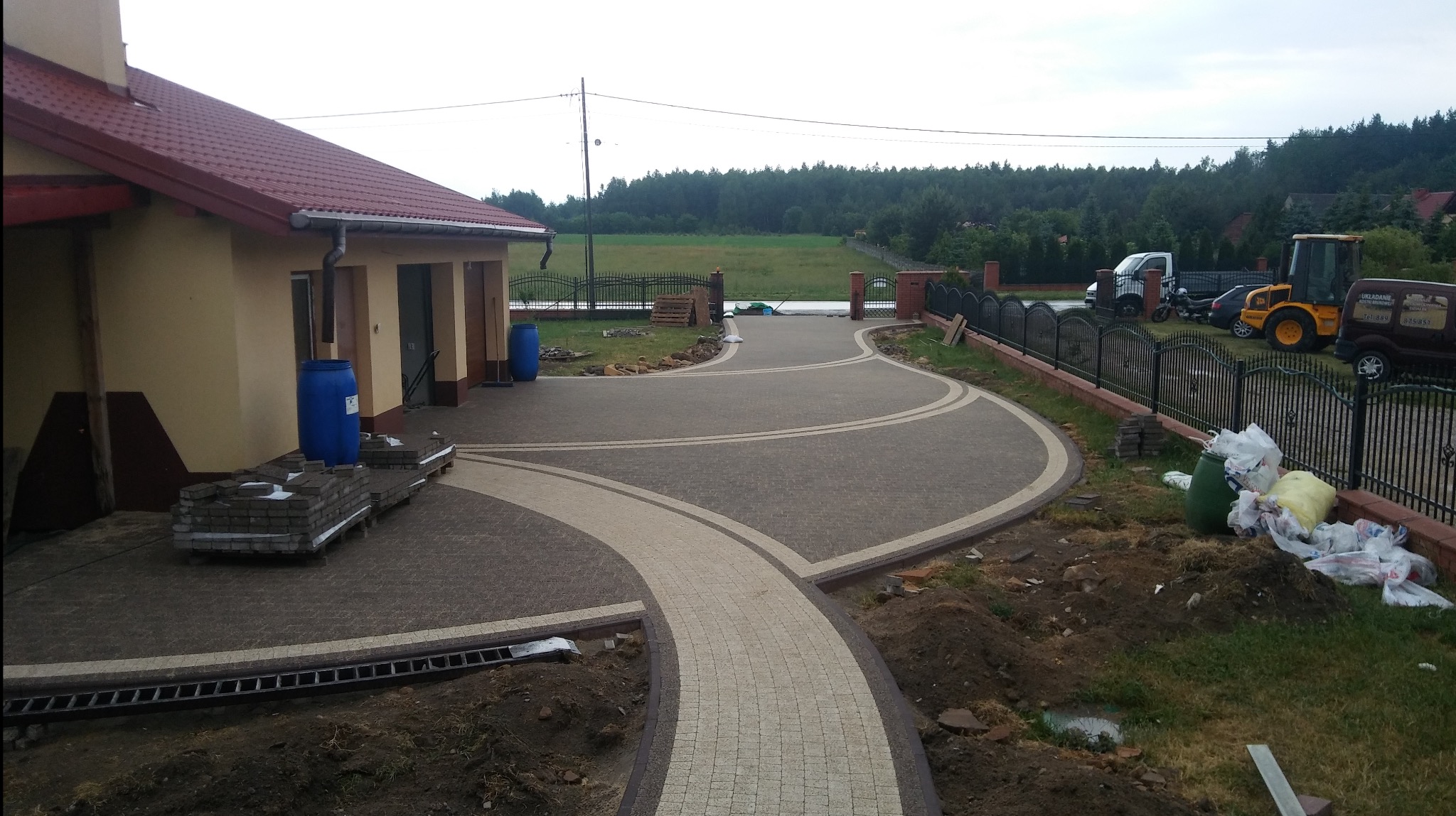 Ułożona z kostki brukowej, zakrzywiona ścieżka prowadząca do domu w Szydłowcu, z widocznymi paletami kostki i elementami krajobrazu w tle.