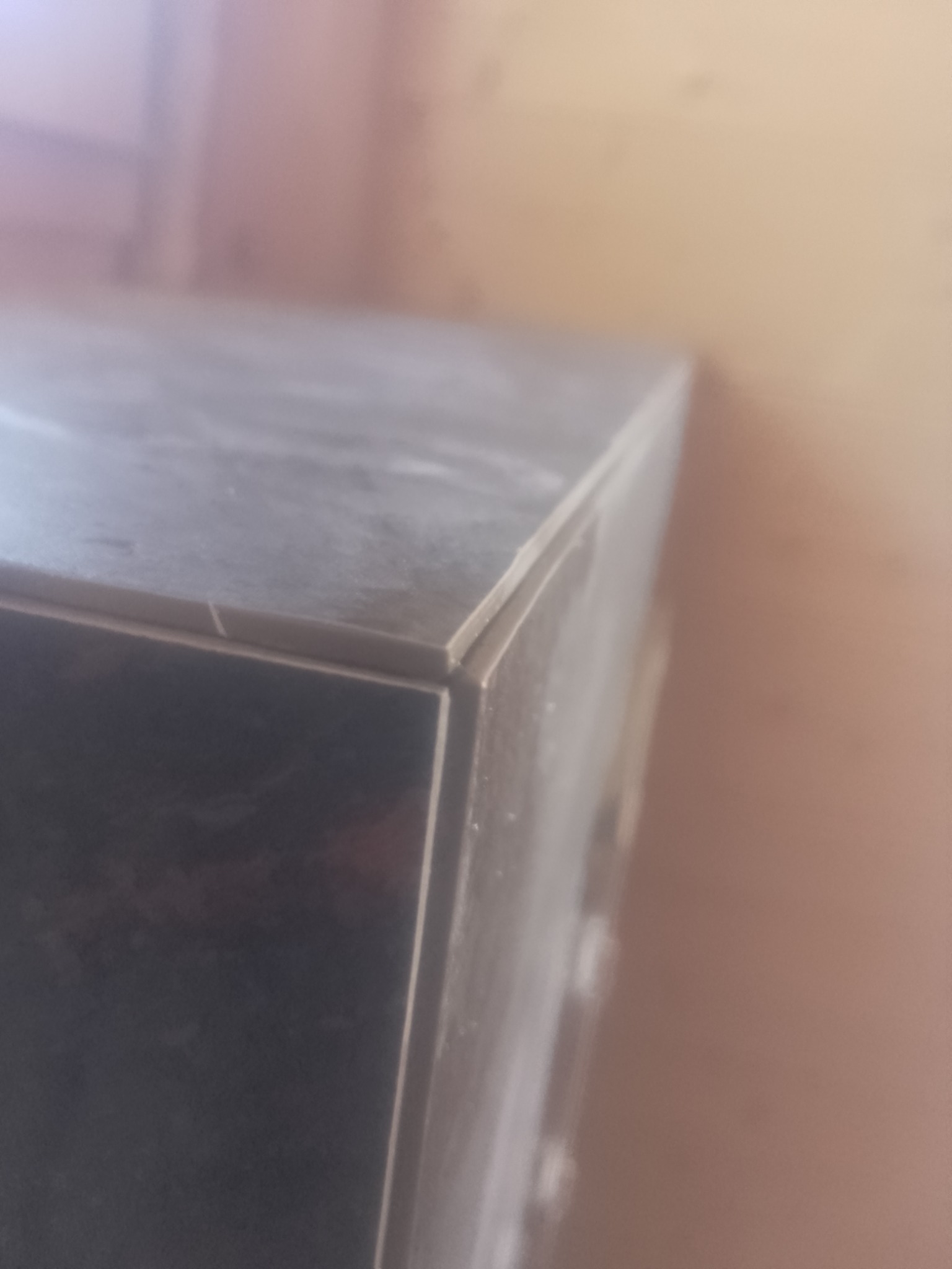 Szczegółowe ujęcie narożnika blatu z ciemnego kamienia lub płytek, widoczne łączenie elementów, lekko zakurzone.