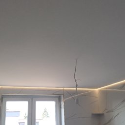 Antoni Przybylski - Nowoczesne oświetlenie LED wzdłuż sufitu i ściany wykończonej płytkami imitującymi marmur. Widoczne okno i wystający kabel od oświetlenia.