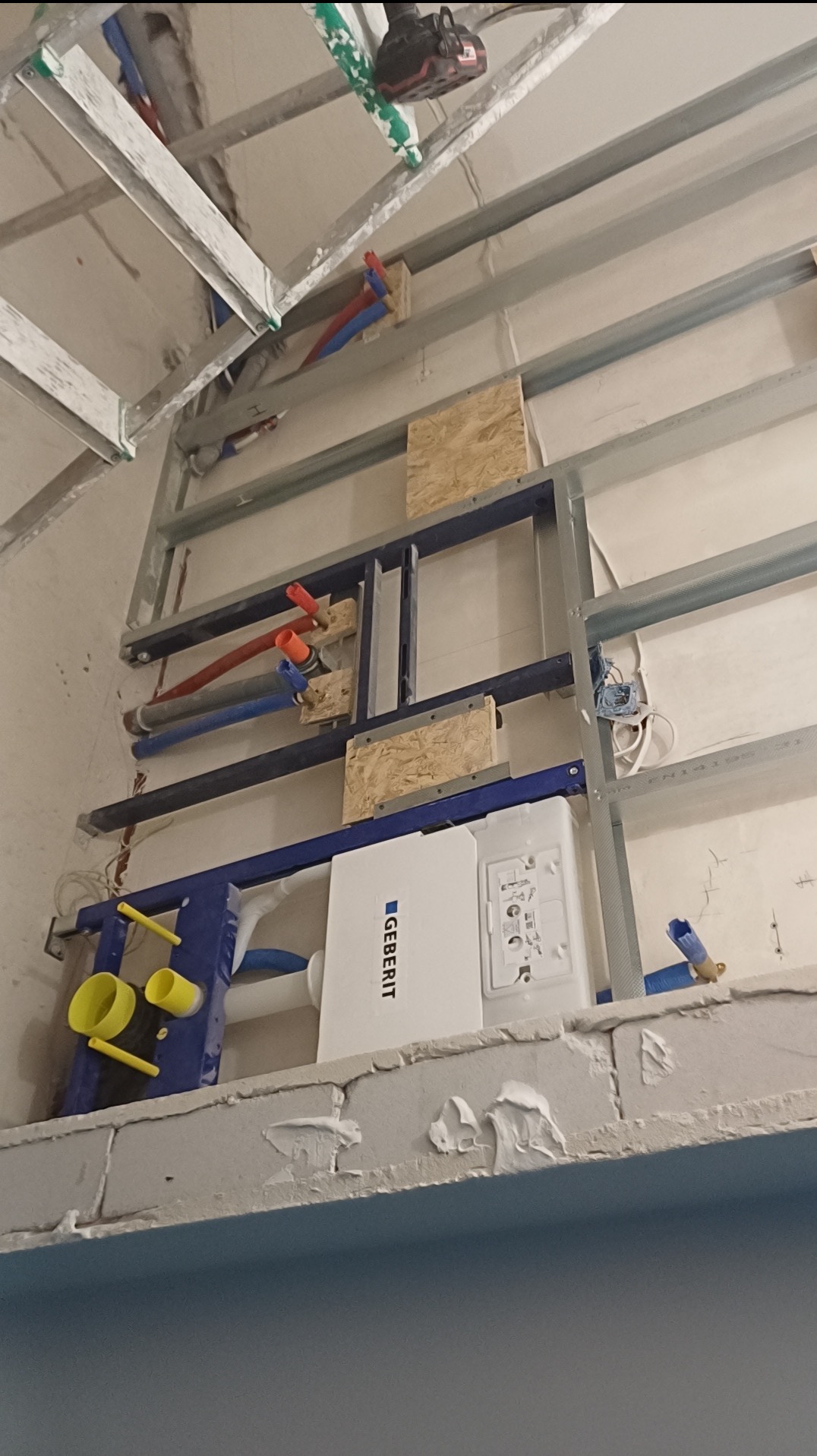 Stelaż podtynkowy Geberit zamontowany w łazience, widoczne rury instalacyjne i metalowa konstrukcja pod zabudowę. Prace instalacyjne w toku, surowy stan.