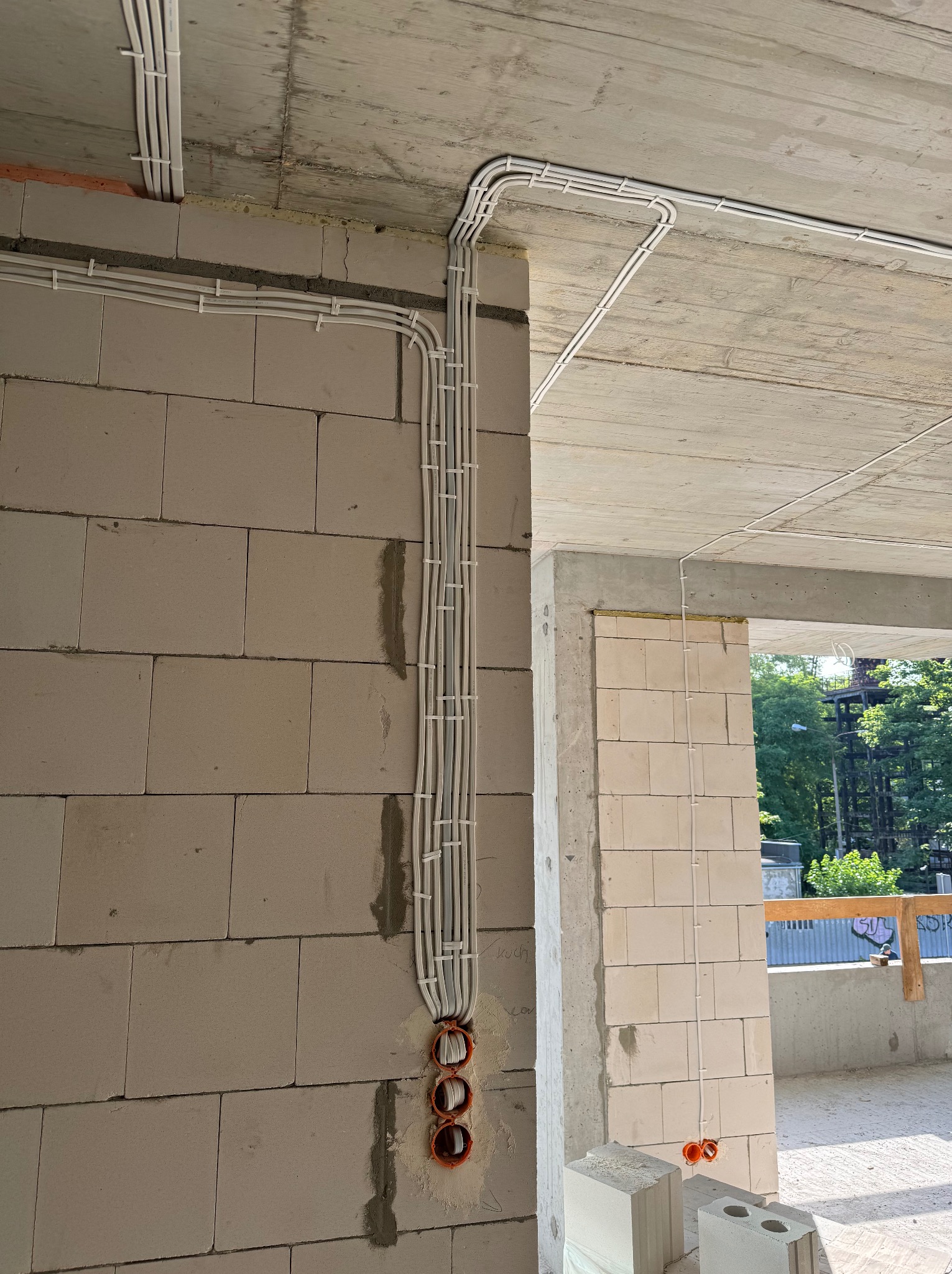 Wewnętrzna instalacja elektryczna w surowym stanie: białe kable prowadzone po ścianie z betonu komórkowego, przymocowane uchwytami, widoczne puszki instalacyjne w ścianie.