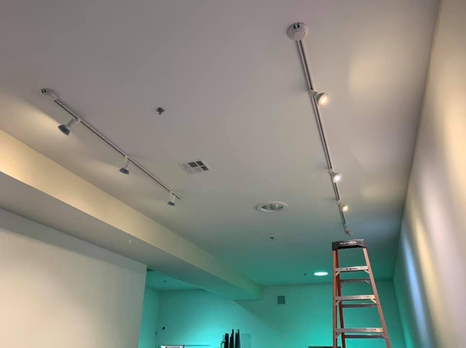 Szyna oświetleniowa z reflektorami zamontowana na suficie, widoczna drabina malarska, sufit z wbudowanymi światłami i czujnikiem dymu.