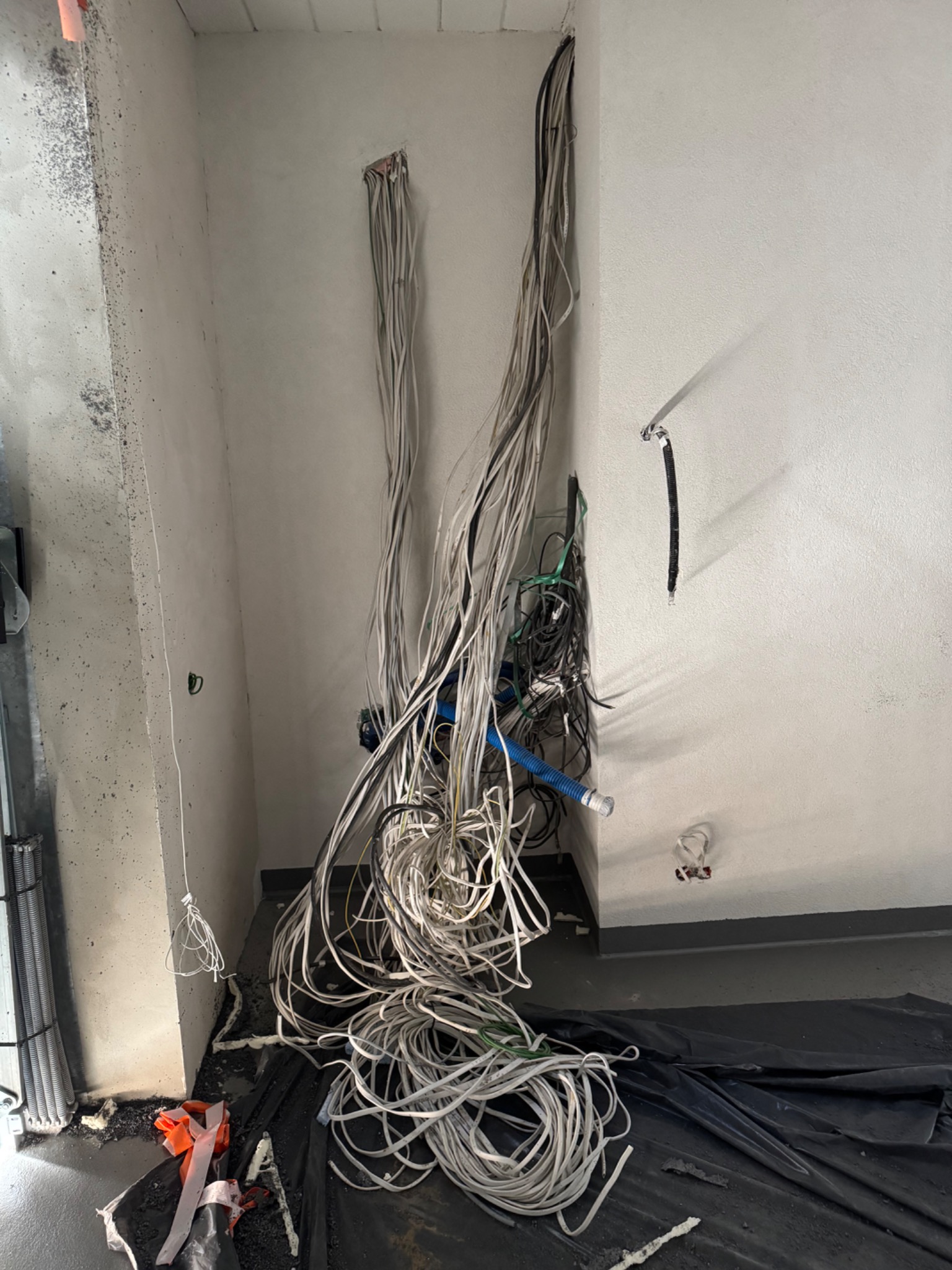 Nieuporządkowane przewody elektryczne zwisające ze ściany w trakcie prac instalacyjnych w pomieszczeniu w Warszawie, widoczne zabezpieczenia podłogi folią.