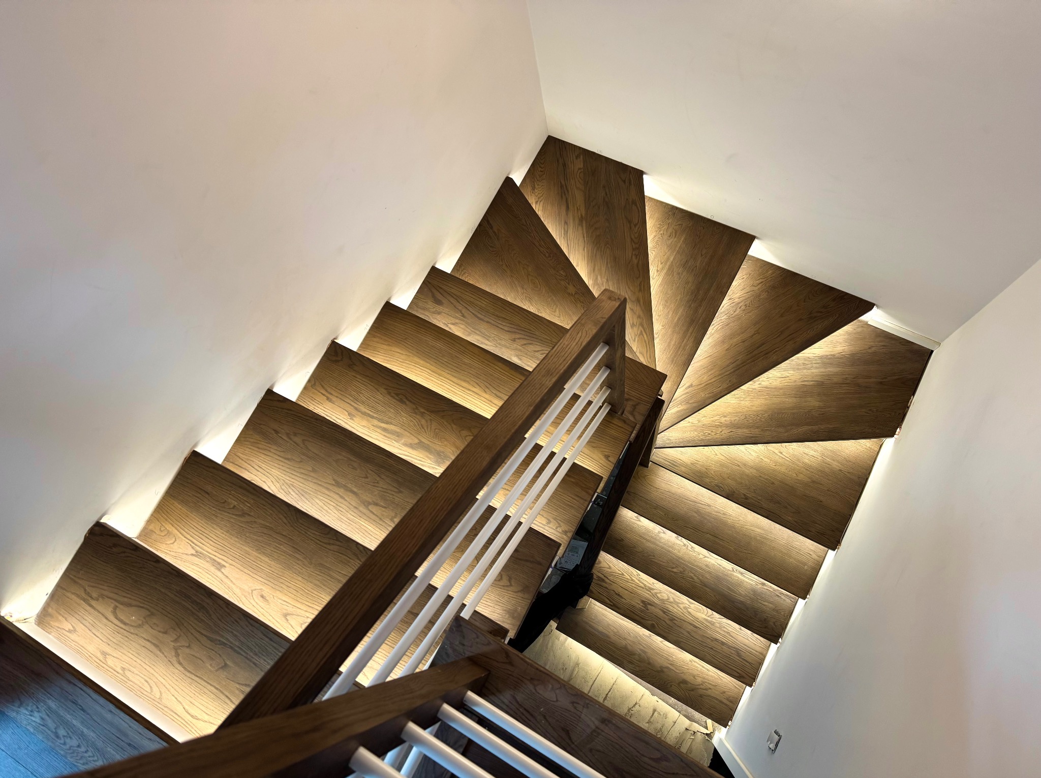 Drewniane schody z nowoczesnym oświetleniem LED pod każdym stopniem, widok z góry, białe ściany, eleganckie wykończenie. Unikalny design oświetlenia schodów.