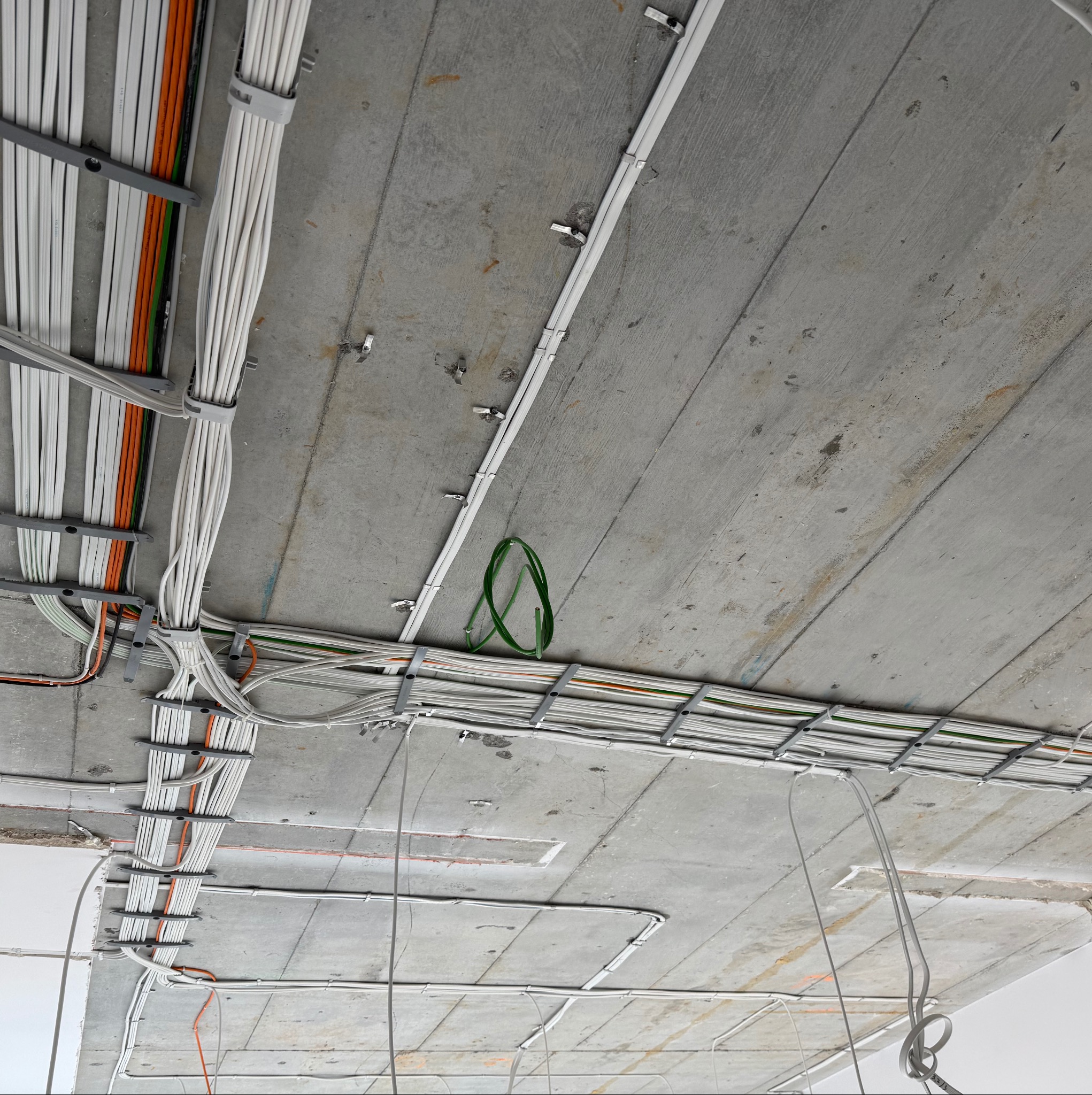 Sufit z surowego betonu z zamocowanymi przewodami elektrycznymi w korytach kablowych. Widoczne kable w różnych kolorach, uporządkowane i przymocowane do sufitu.