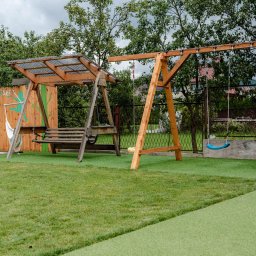 Restauracja Food Makerzy Kluszkowce - Drewniany plac zabaw z huśtawkami i hamakiem na zielonej trawie, ogrodzony drewnianym płotem z malunkami.