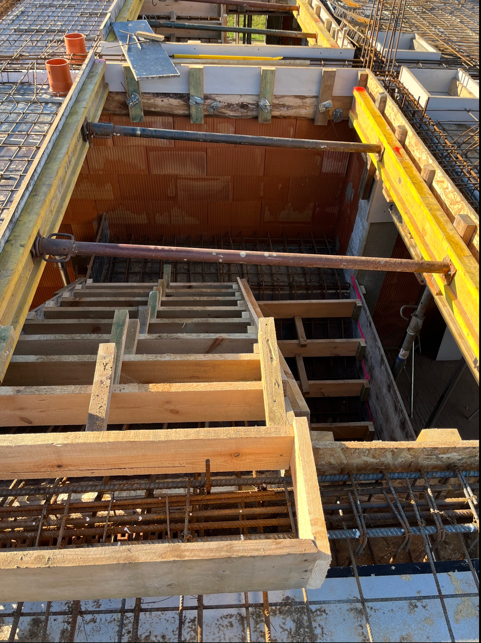 Wnętrze szalunku stropowego z widoczną konstrukcją z belek drewnianych, stalowym zbrojeniem i pustakami ceramicznymi, przygotowane do zalewania betonem.