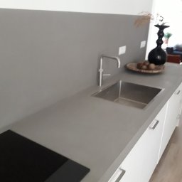 KRIS-STUC Krystian Maczukin - Szara, minimalistyczna kuchnia w Grudziądzu z blatem zlewem i płytą grzewczą, wykończona gładzią na ścianie w odcieniu szarości.