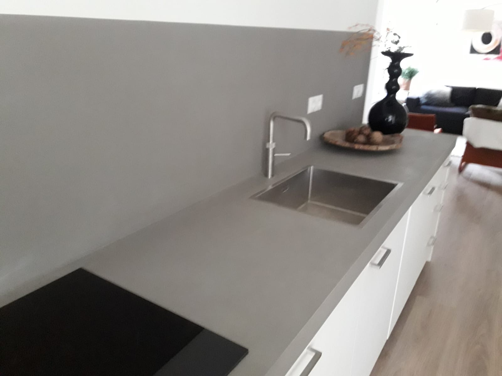 Szara, minimalistyczna kuchnia w Grudziądzu z blatem zlewem i płytą grzewczą, wykończona gładzią na ścianie w odcieniu szarości.