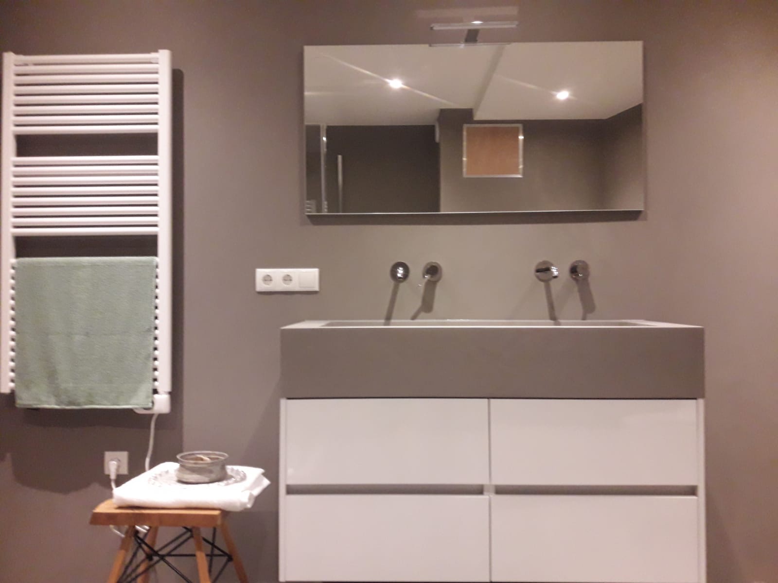 Nowoczesna łazienka w odcieniach szarości z podwójną umywalką, grzejnikiem drabinkowym z zielonym ręcznikiem i lustrem z widocznym odbiciem sufitu.