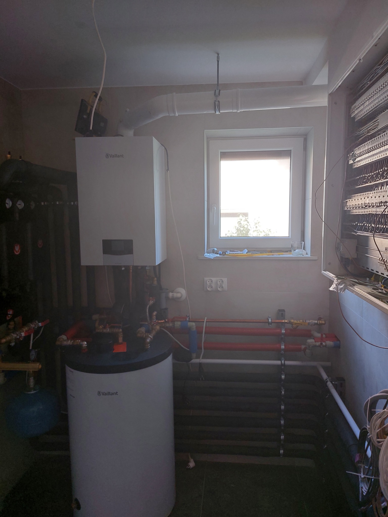 Piec gazowy Vaillant z podłączonym zasobnikiem CWU w kotłowni w Drwini, widoczne rury instalacji grzewczej i elektryczna skrzynka sterownicza.