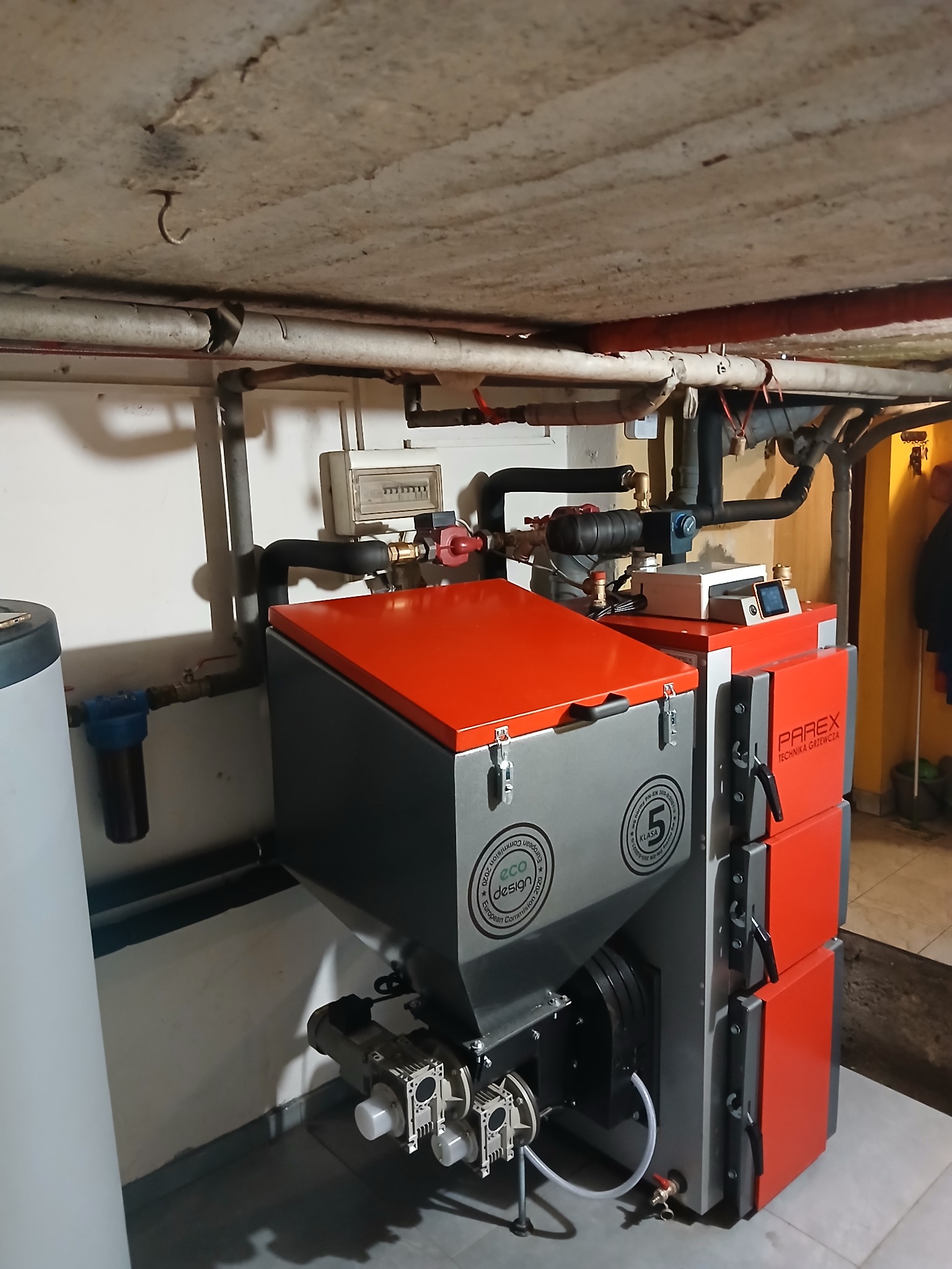 Szaro-czerwony piec CO marki Parex w kotłowni, widoczne rury instalacji grzewczej pod sufitem