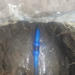 MARLIN DEEP SOLUTIONS Volodymyr Balandin - Niebieska rura wodociągowa z łącznikiem, zakopana w wykopie ziemnym z widocznymi korzeniami