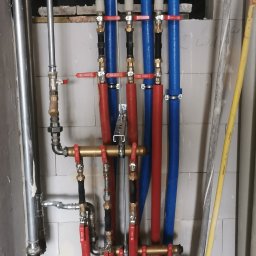 MARLIN DEEP SOLUTIONS Volodymyr Balandin - Złożona instalacja hydrauliczna z rurami w kolorach czerwonym i niebieskim, zaworami i elementami mocującymi, zamontowana na tle surowej ściany z pustaków.