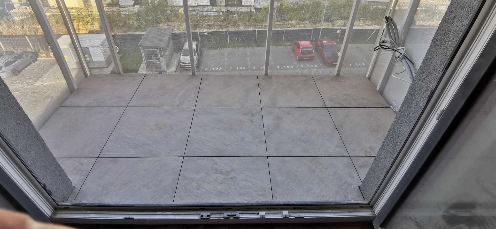 Wykończony balkon z szarymi płytkami w Katowicach, widok z góry na parking. Widoczne kable i elementy konstrukcyjne.