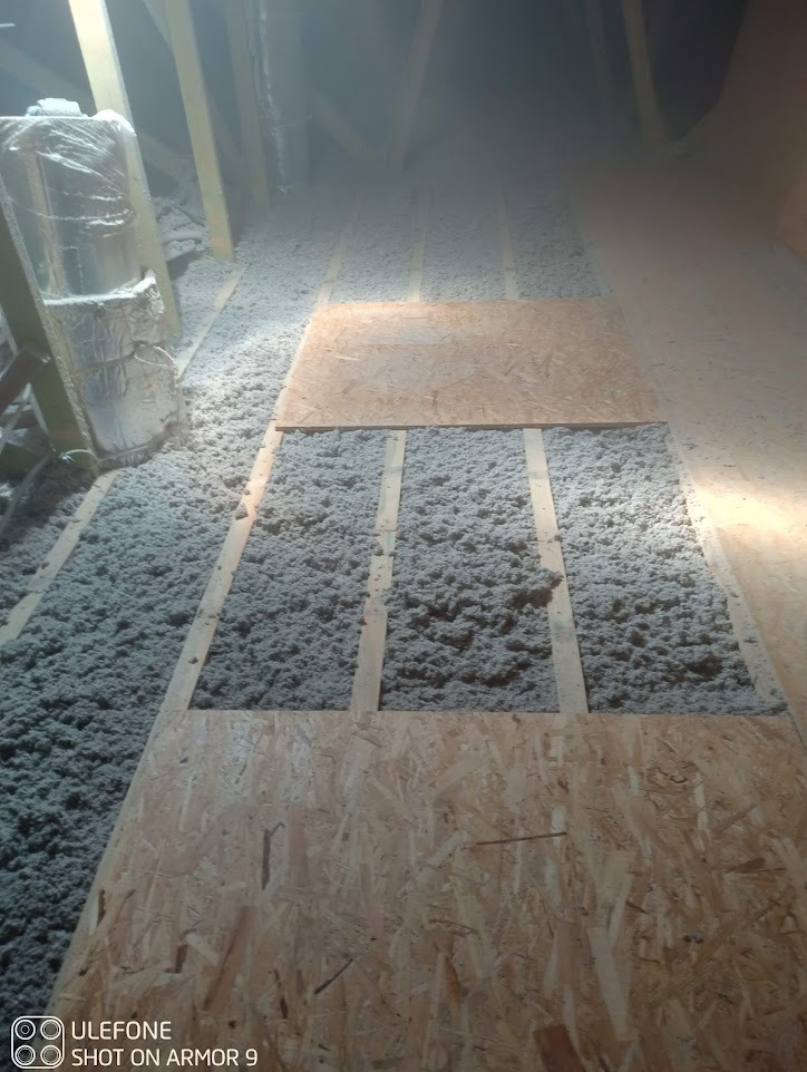 Poddasze w trakcie izolacji: wełna mineralna wypełnia przestrzeń między krokwiami, częściowo przykryta płytami OSB, widoczne elementy konstrukcji drewnianej dachu.