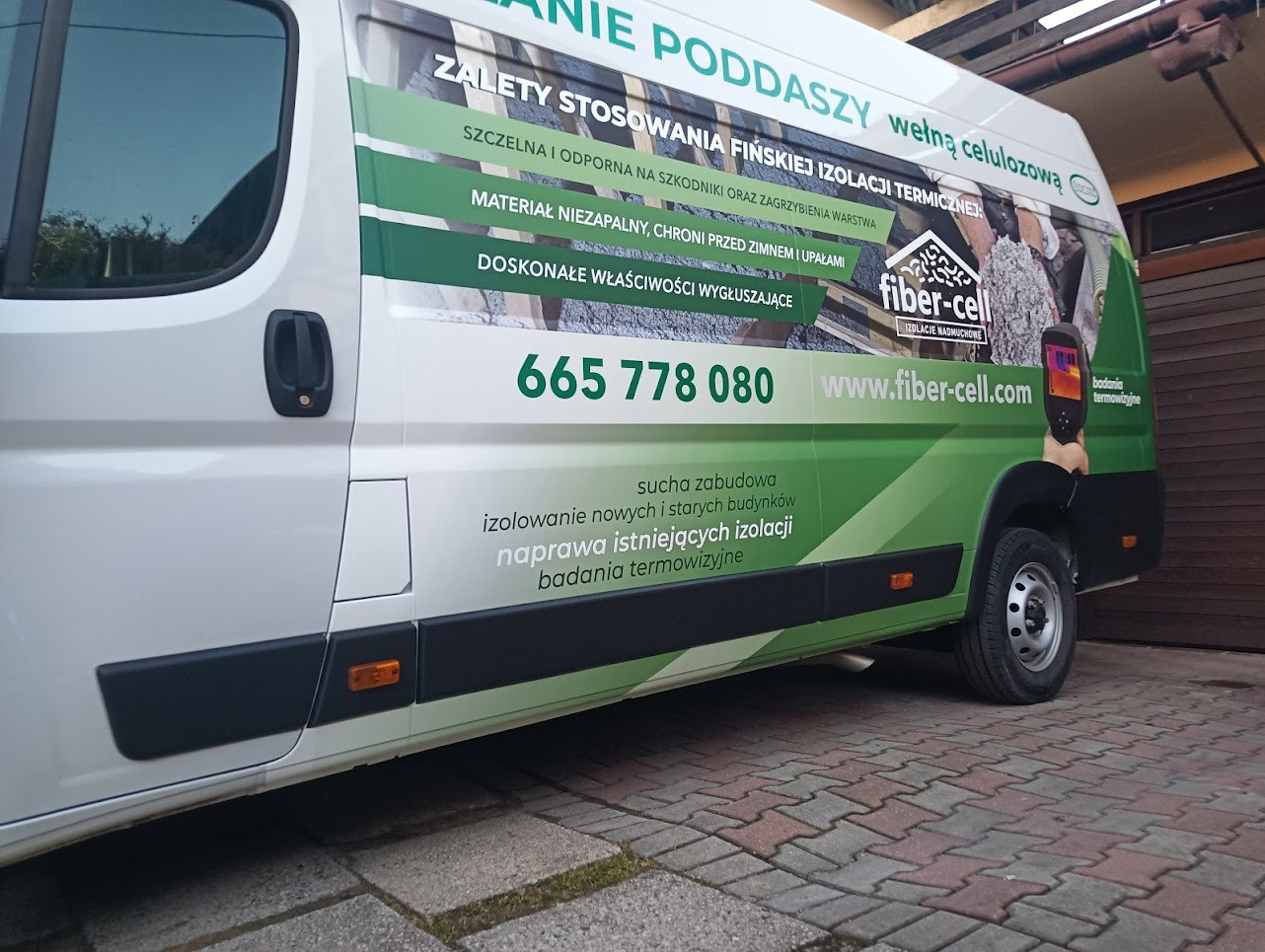Biały samochód dostawczy z reklamą izolacji termicznej Fiber-Cell, prezentujący zalety stosowania wełny celulozowej do ocieplania poddaszy, z widocznym numerem telefonu i adresem strony...
