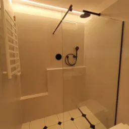 Nowoczesna kabina prysznicowa z czarną armaturą i białymi płytkami z czarnymi akcentami na podłodze, oświetlenie LED pod sufitem.