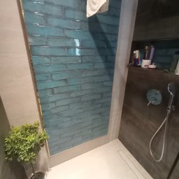 FERMONT USŁUGI BUDOWLANE Wojciech Nowak - Nowoczesna kabina prysznicowa z turkusowymi, błyszczącymi płytkami ułożonymi w cegiełkę, szara ściana, biała posadzka z odpływem liniowym, roślina doniczkowa w rogu, półka z kosmetykami i słuchawka...