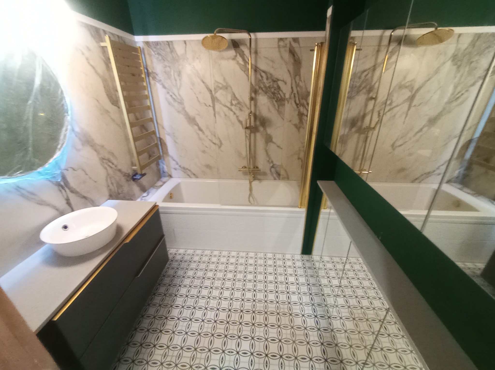 Nowoczesna łazienka z marmurowymi płytkami, złotą armaturą, umywalką nablatową i wzorzystą podłogą.