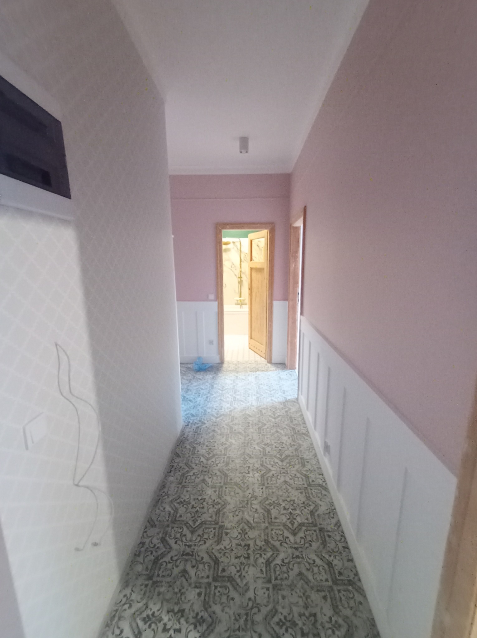 Wykończony korytarz w pastelowych kolorach z wzorzystą podłogą i białymi panelami ściennymi, widok na otwarte drzwi do łazienki.