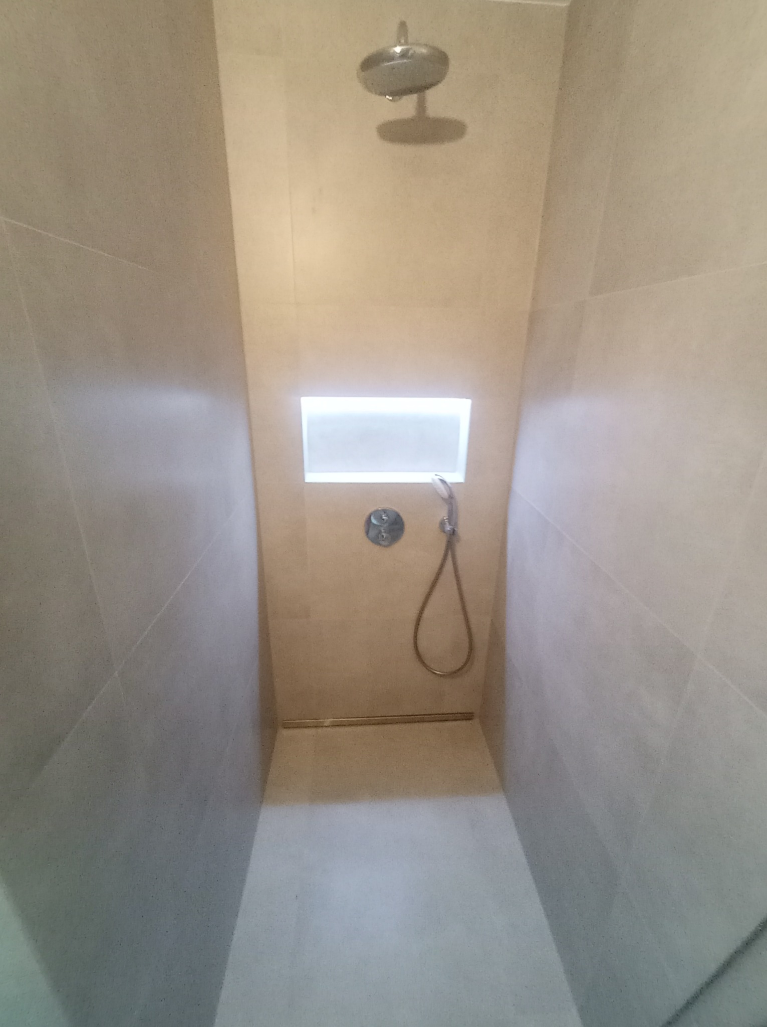 Nowoczesna kabina prysznicowa z beżowymi płytkami, deszczownicą, wnęką z podświetleniem LED i odpływem liniowym.